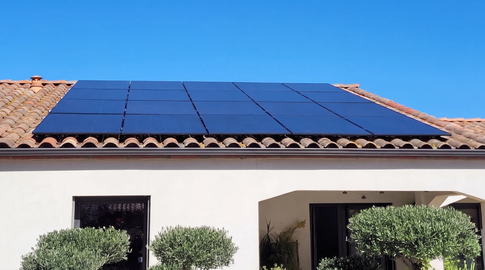 Vue en plongée d'une toiture de maison résidentielle moderne équipée de panneaux solaires photovoltaïques bleus-noirs, installation complète et professionnelle, avec un ciel partiellement nuageux. La toiture doit occuper la majorité du cadre, montrant clairement les modules photovoltaïques installés, les fixations métalliques, et idéalement un ou deux panneaux supplémentaires légèrement décalés pour illustrer la dimension de l'installation.